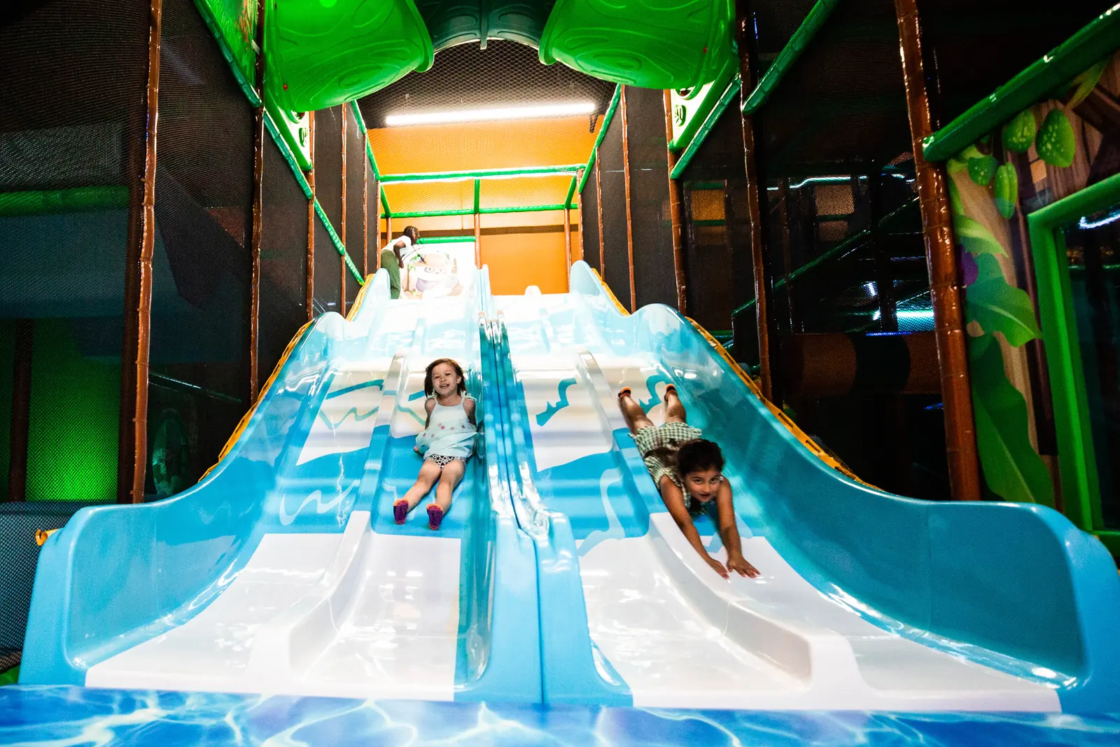 Two children racing side by side down the wide indoor slides