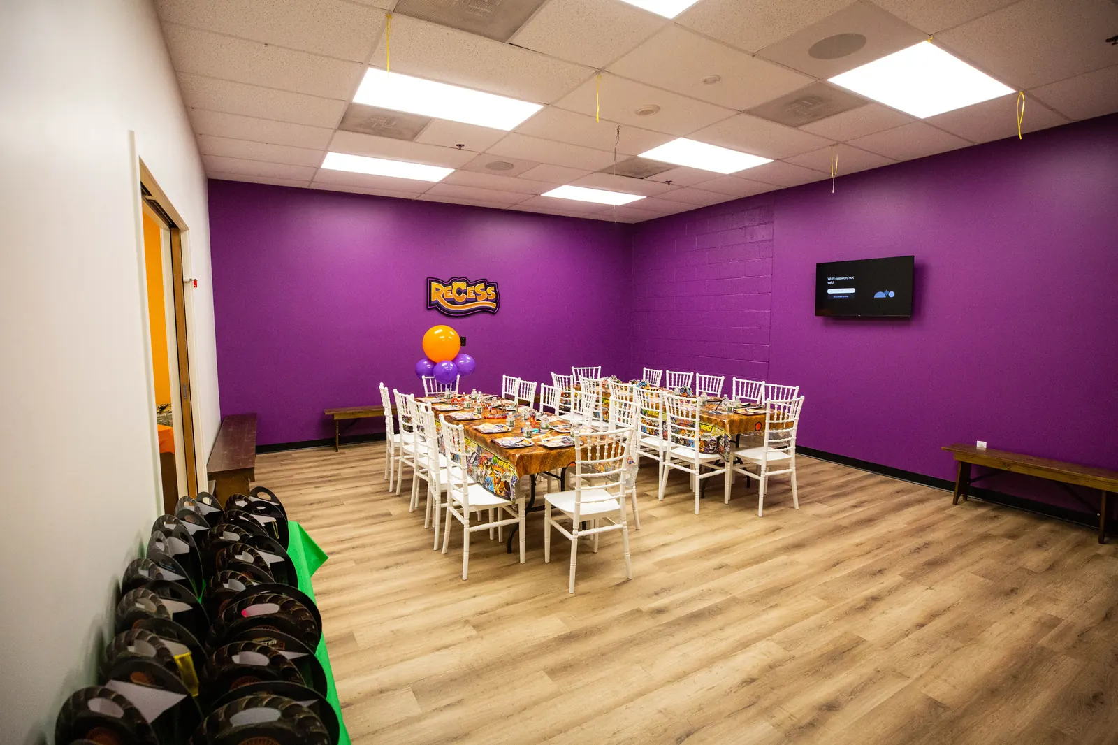 A decorated party room set up with tables and balloons at Recess