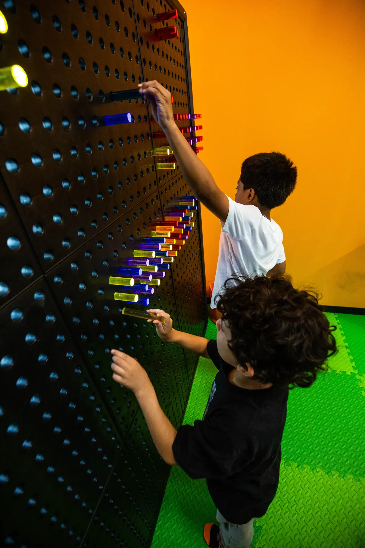 Two children reaching up to play on a pegboard climbing wall