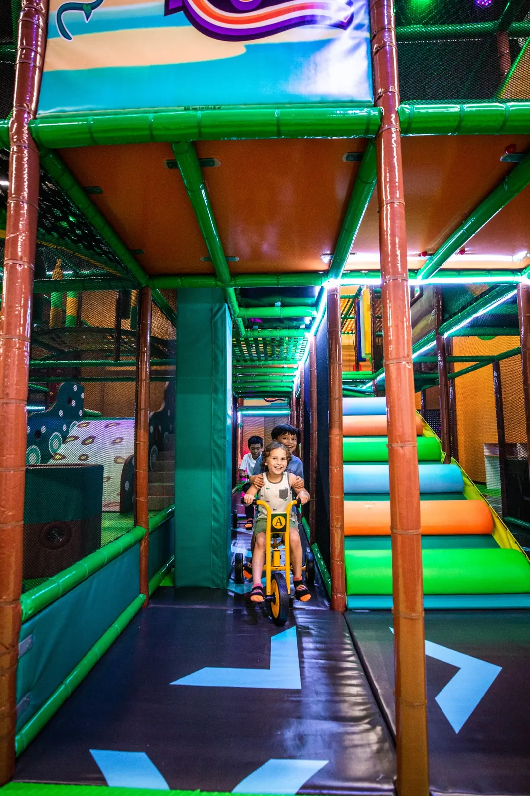 Children riding trikes together through the indoor play area